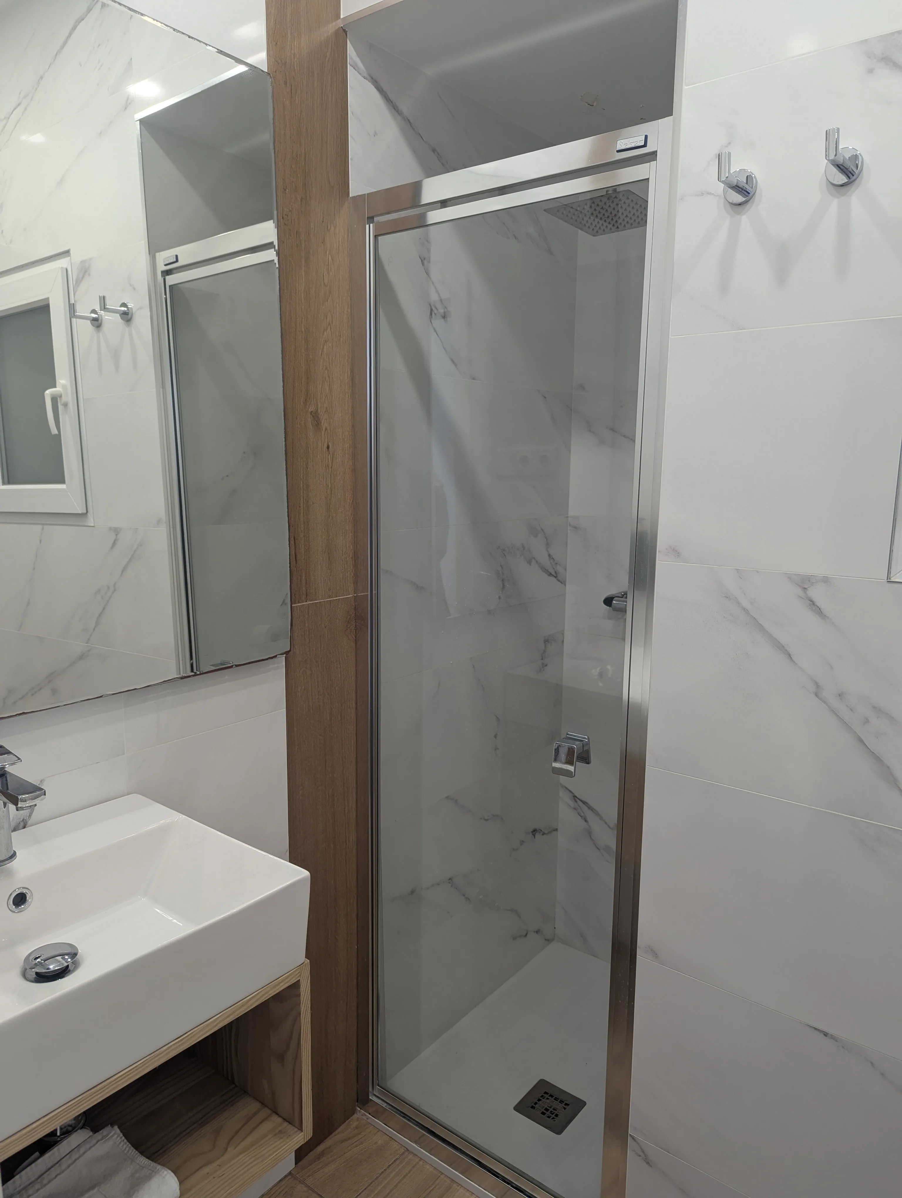 Baño con mármol blanco y madera en habitación doble con vistas de Hostal La Mexicana