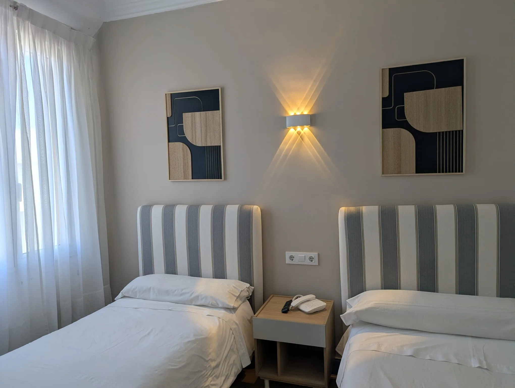 Habitación doble económica de Hostal La Mexicana con aplique de pared encendido y cabeceros tapizados de rayas