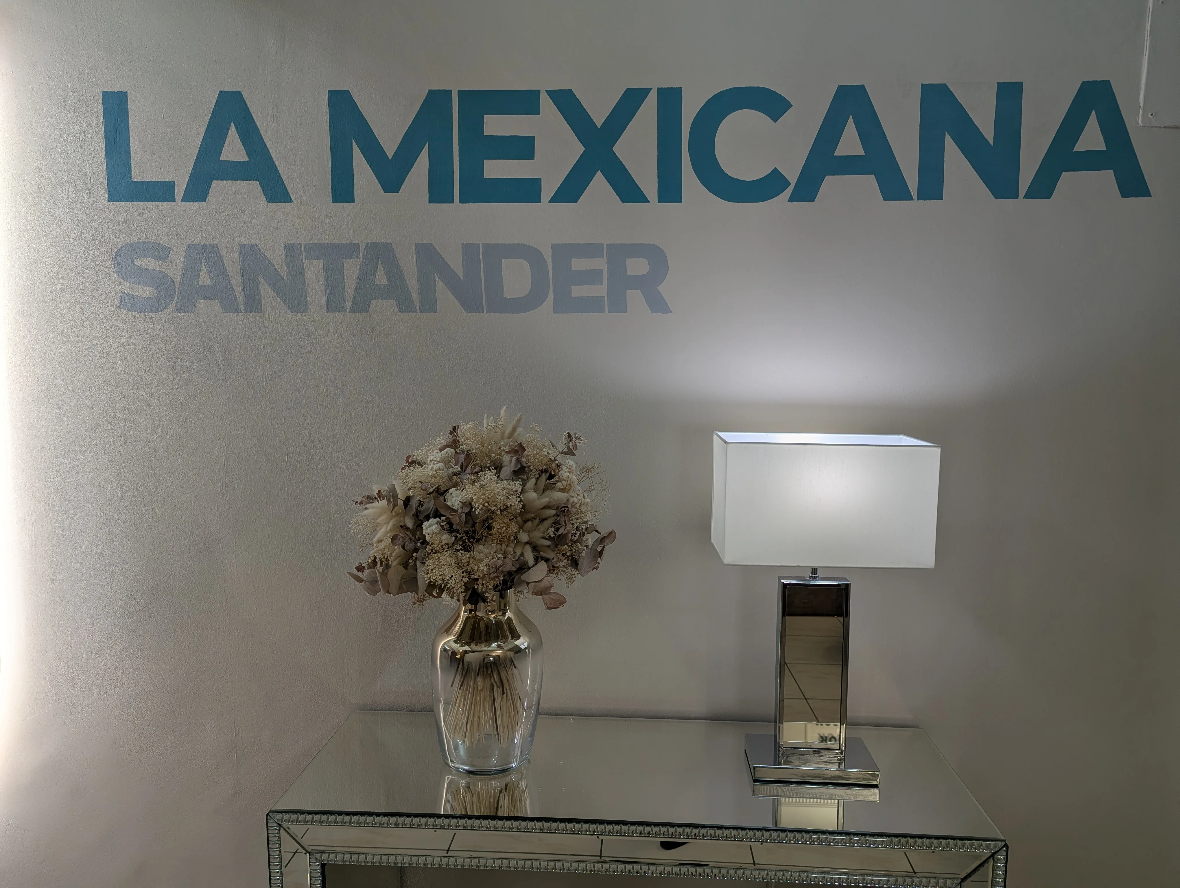 Letrero La Mexicana Santander con consola de espejo, flores y lámpara en la recepción