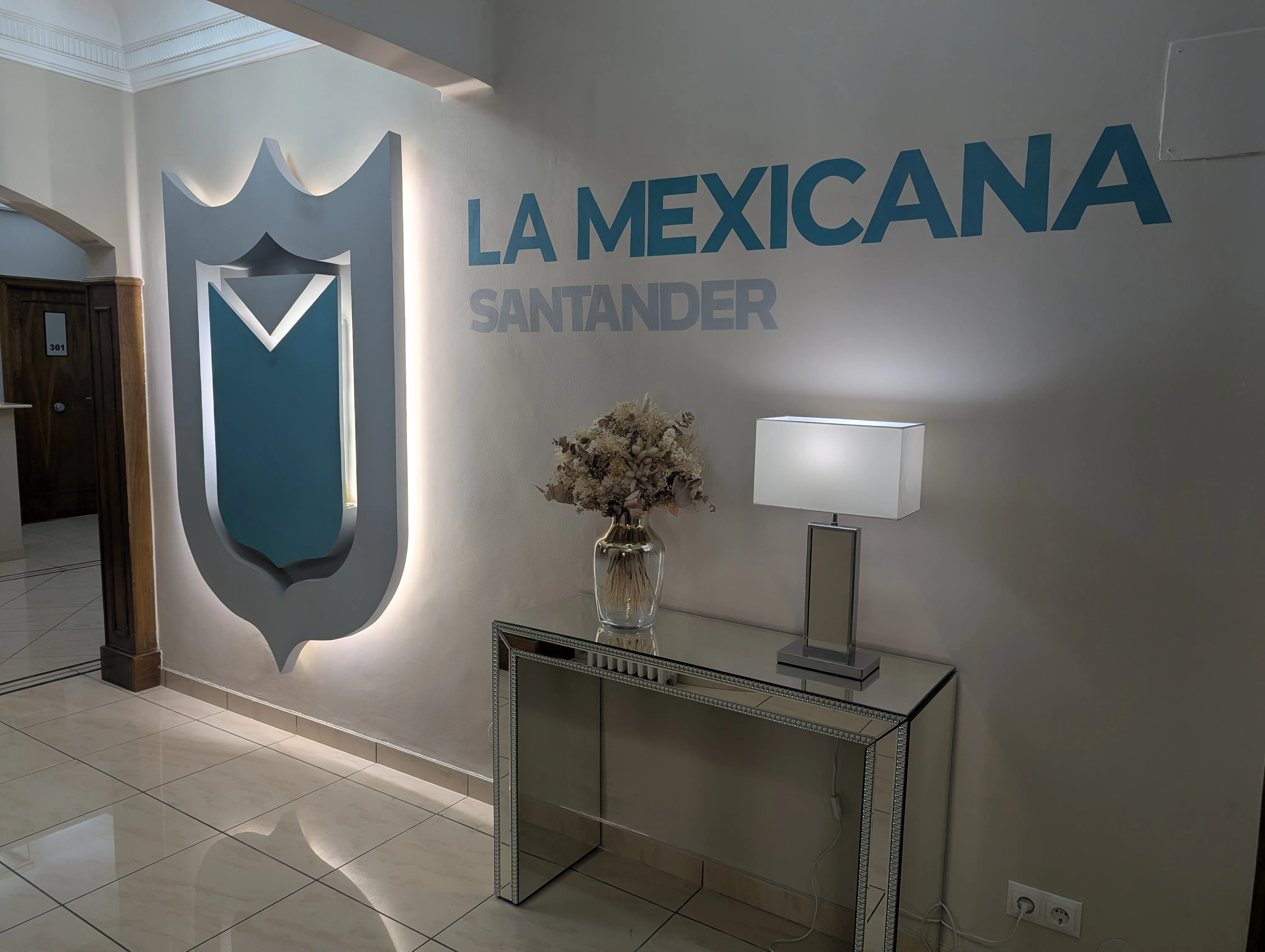 Recepción de Hostal La Mexicana en Santander con escudo iluminado y consola de espejo